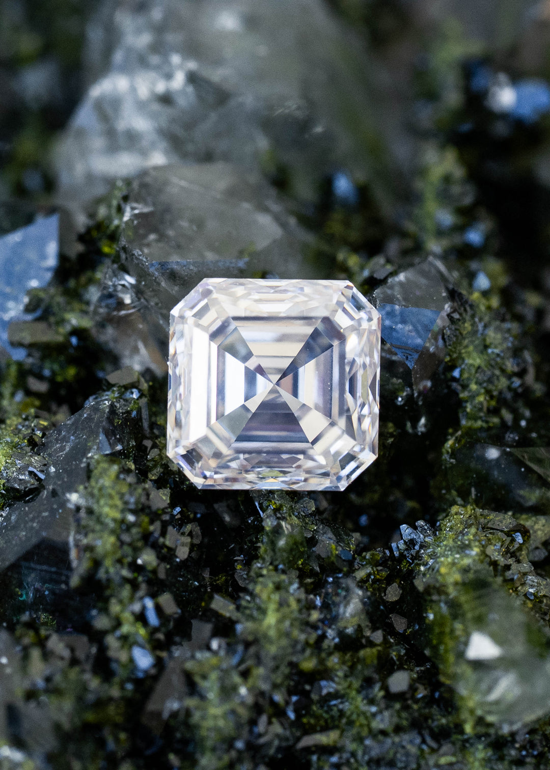 1.01 carat M color VVS1 Asscher cut Canadian diamond displayed on dark green mineral crystals, showing its clipped corners and bold symmetrical step-facet pattern.