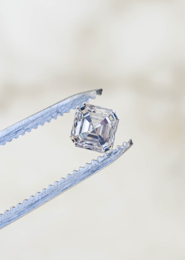 Angled macro view of the 1.01 carat Asscher cut Canadian diamond held in jeweler’s tweezers, showing its depth, clipped corners and layered step facets.