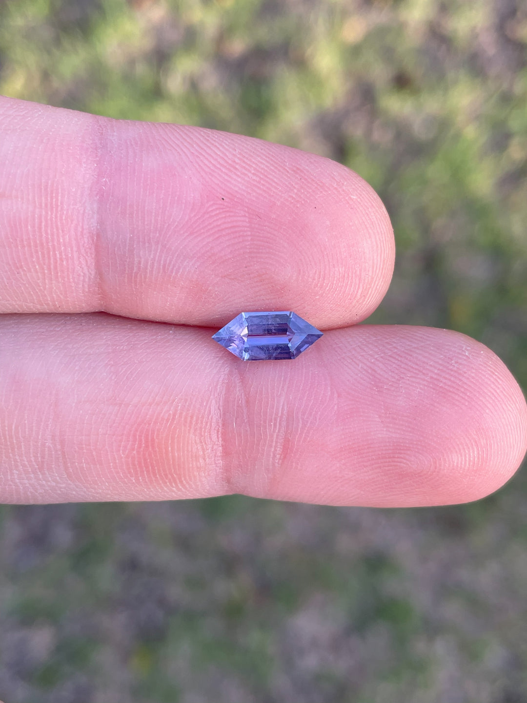 A stunning 1.01-carat hexagon step-cut sapphire with royal purple and pink hues, ethically sourced from Madagascar, displayed on a fingertip.