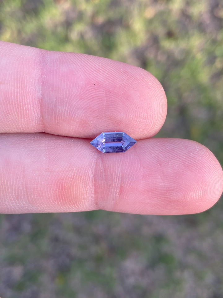 A stunning 1.01-carat hexagon step-cut sapphire with royal purple and pink hues, ethically sourced from Madagascar, displayed on a fingertip.
