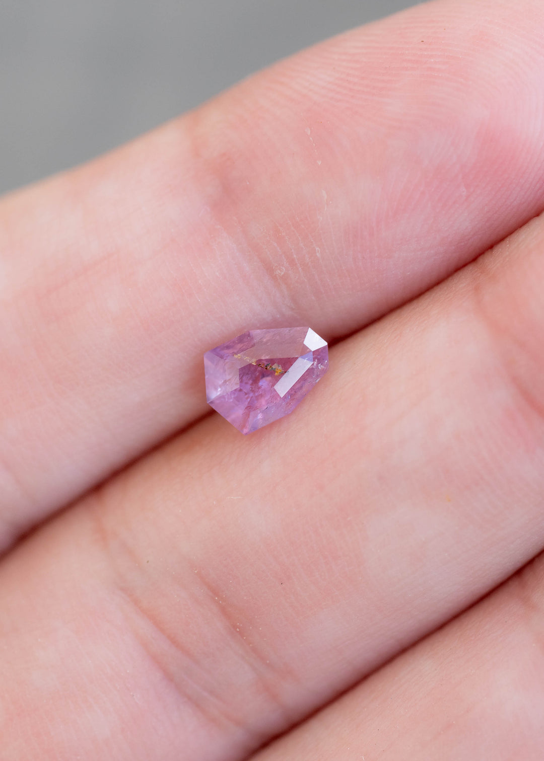 Natural untreated 1.01 carat soft rose pink sapphire from Rio Mayo, Mercaderes, Colombia displayed on fingertips for scale, showcasing its custom shield mix cut and delicate pastel color.