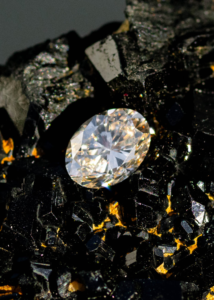 1.01ct champagne c3 oval brilliant cut diamond resting on natural tourmaline gemstone under direct sunlight.