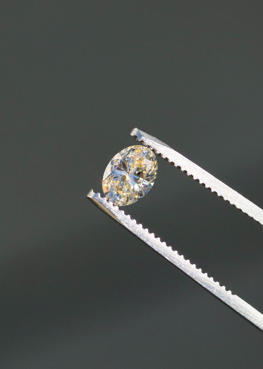1.01ct champagne c3 oval brilliant cut diamond held in gem tweezers under direct sunlight showing off color and sparkle.