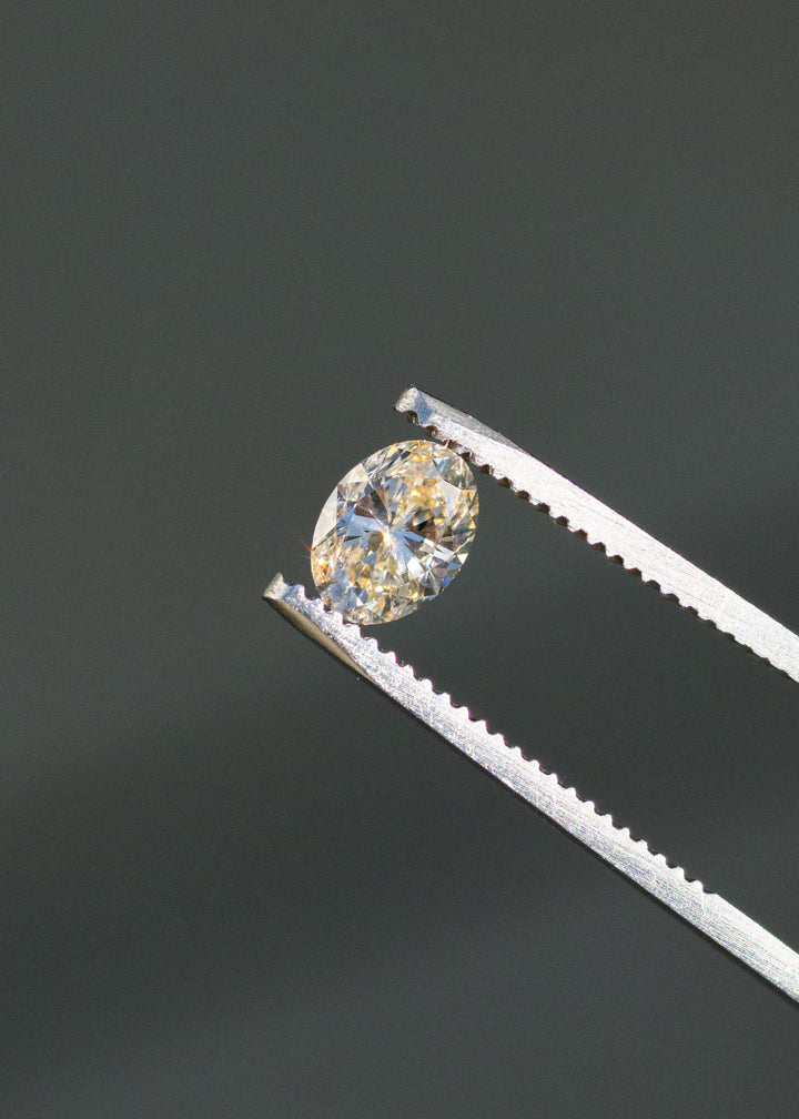 1.01ct champagne c3 oval brilliant cut diamond held in gem tweezers under direct sunlight showing off color and sparkle.