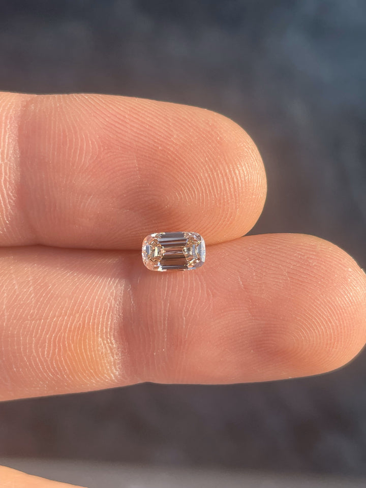 A stunning 1.02-carat antique-style elongated step cut cushion diamond with a champagne hue, photographed on a fingertip to show its elegant proportions and clarity.