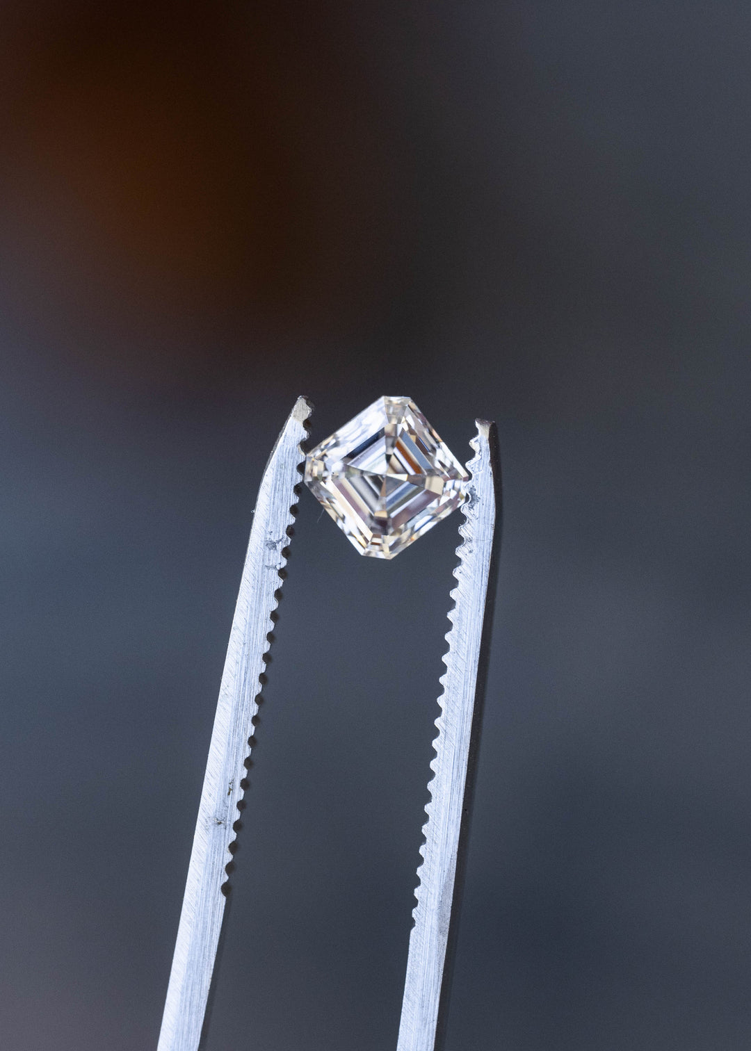 Face-up macro photograph of a 1.02 carat natural Asscher cut diamond on a pale background, showing its nearly square proportions and crisp hall-of-mirrors facet pattern.