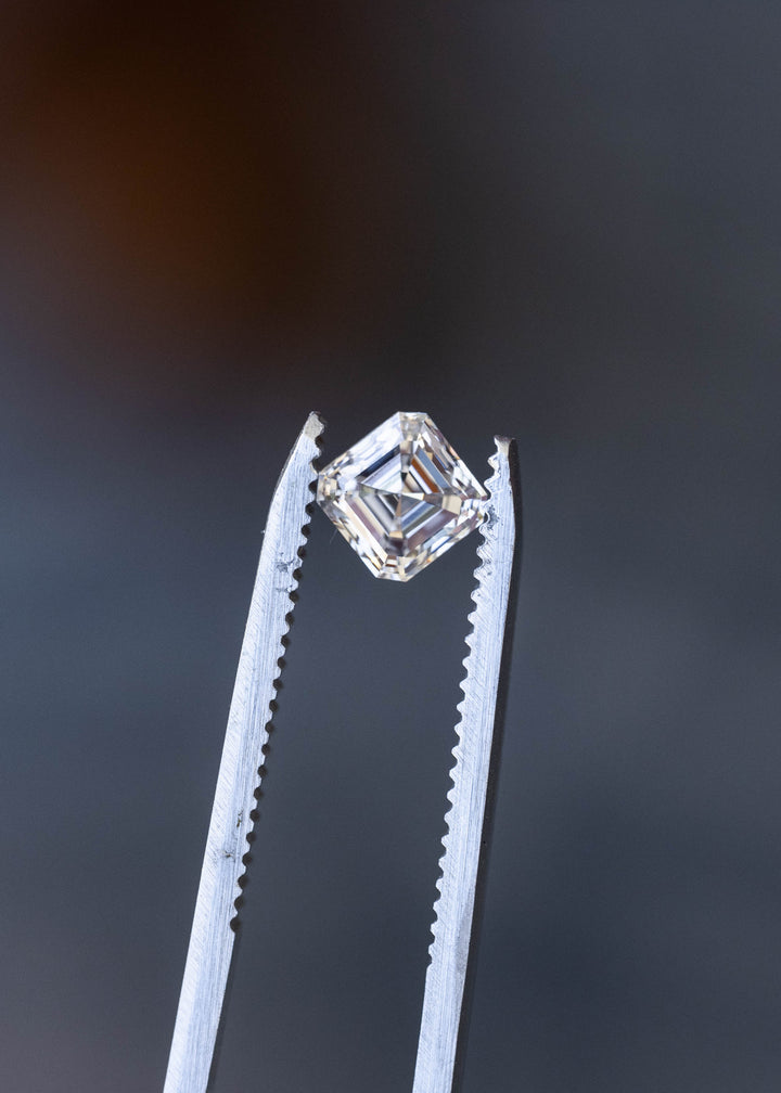 Face-up macro photograph of a 1.02 carat natural Asscher cut diamond on a pale background, showing its nearly square proportions and crisp hall-of-mirrors facet pattern.