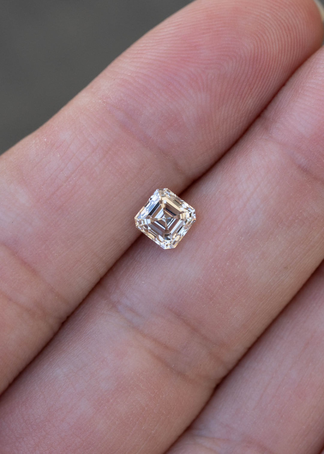 1.02 carat M color VVS1 Asscher cut diamond resting on a hand for scale, displaying pale champagne warmth and strong geometric reflections.