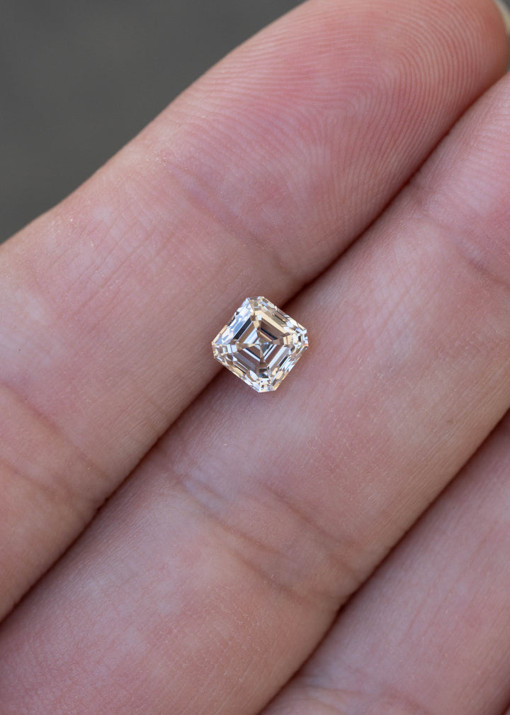 1.02 carat M color VVS1 Asscher cut diamond resting on a hand for scale, displaying pale champagne warmth and strong geometric reflections.