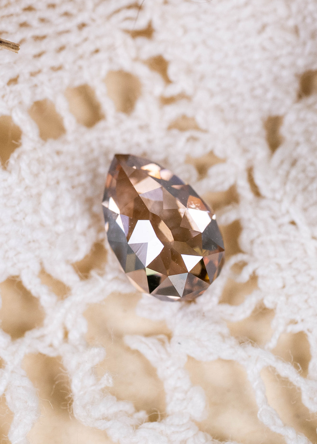 A 1.02ct Fancy Orangish Brown diamond from South Africa, photographed on ivory lace. Its unusual Pear Mughal cut reveals warm cognac tones, broad geometric facets, and distinctive antique-inspired character.