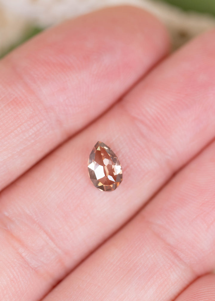 A 1.02ct Fancy Orangish Brown Pear Mughal cut diamond photographed on fingers for scale. Its warm copper and cognac coloration, elongated pear shape, and VVS2 clarity make it a distinctive option for bespoke fine jewelry.