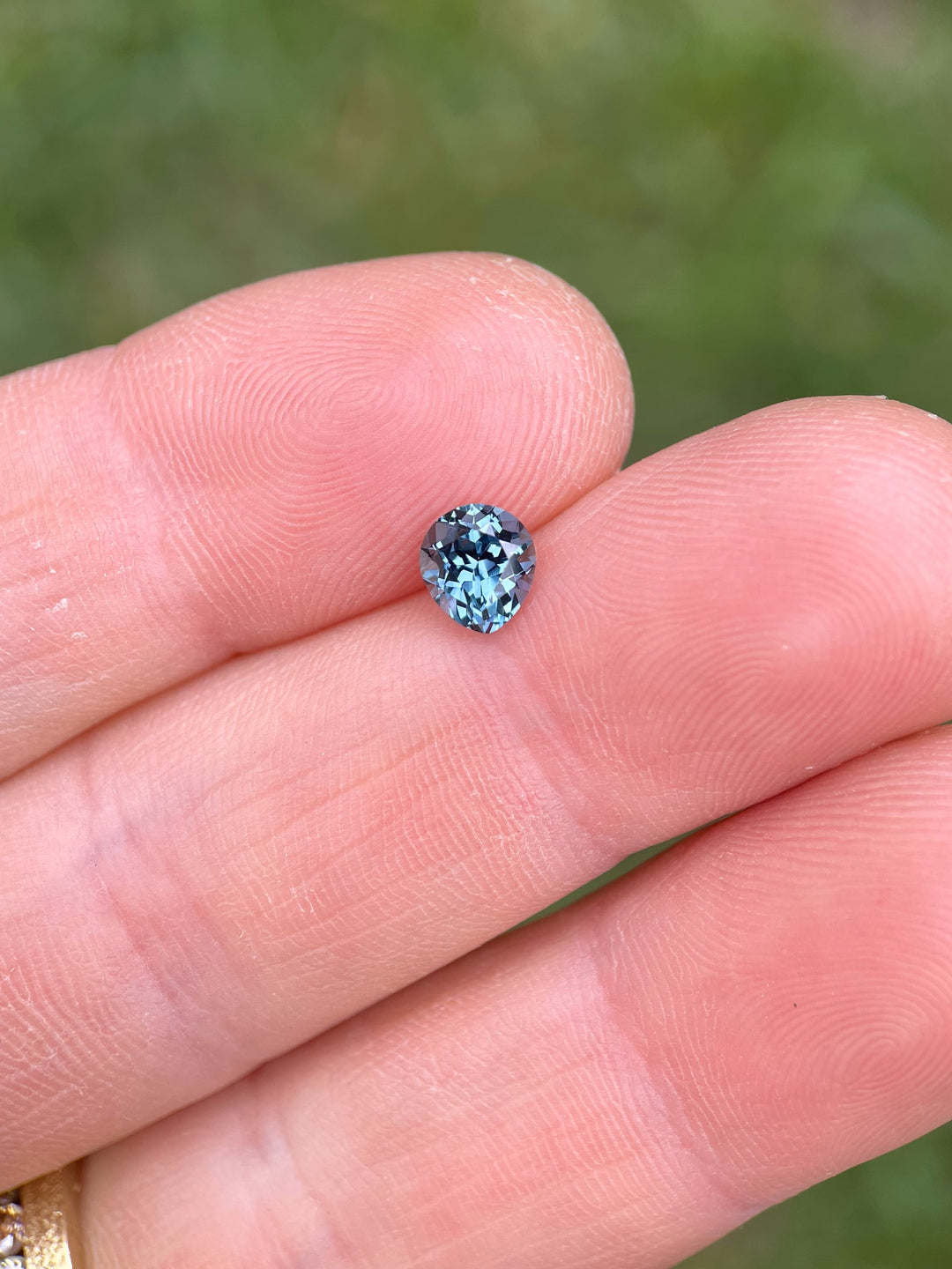 1.02 carat heated Montana sapphire showing teal, blue, and green hues resting on a fingertip.