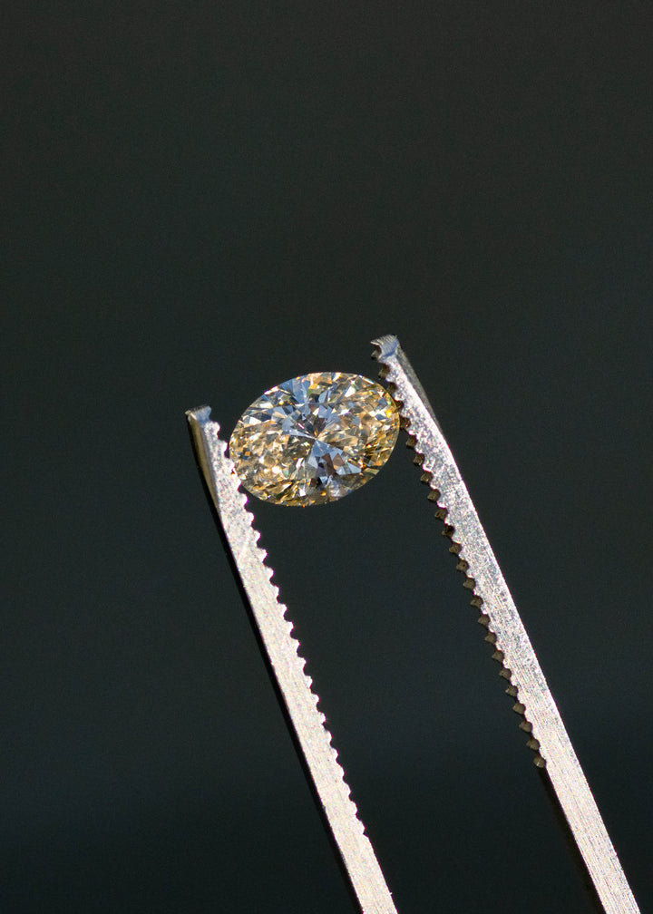 1.02ct natural champagne oval brilliant cut diamond from Canada held in gem tweezers showing off brilliant faceting and warm tones.
