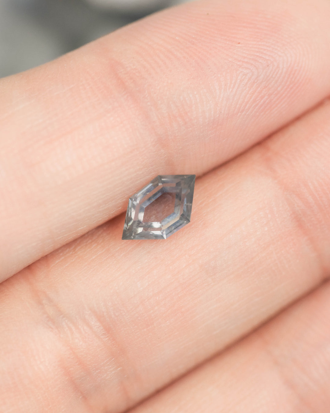 1.03 carat blue purple gray Montana sapphire resting on finger for scale, hexagon portrait tablet cut with step facets, untreated sapphire from El Dorado Bar Deposit.