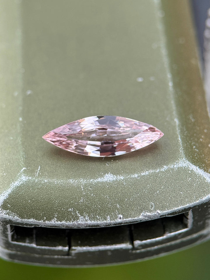 1.03 carat blush pink sapphire resting on a metallic surface, displaying soft pastel pink tones and high brilliance from its precision marquise mixed cut, heated sapphire from Sakaraha, Madagascar.