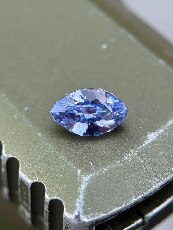 1.03 carat indigo and purple sapphire resting on metallic surface, capturing deep color play and brilliance from its precision marquise mixed cut, untreated sapphire from Sakaraha, Madagascar.