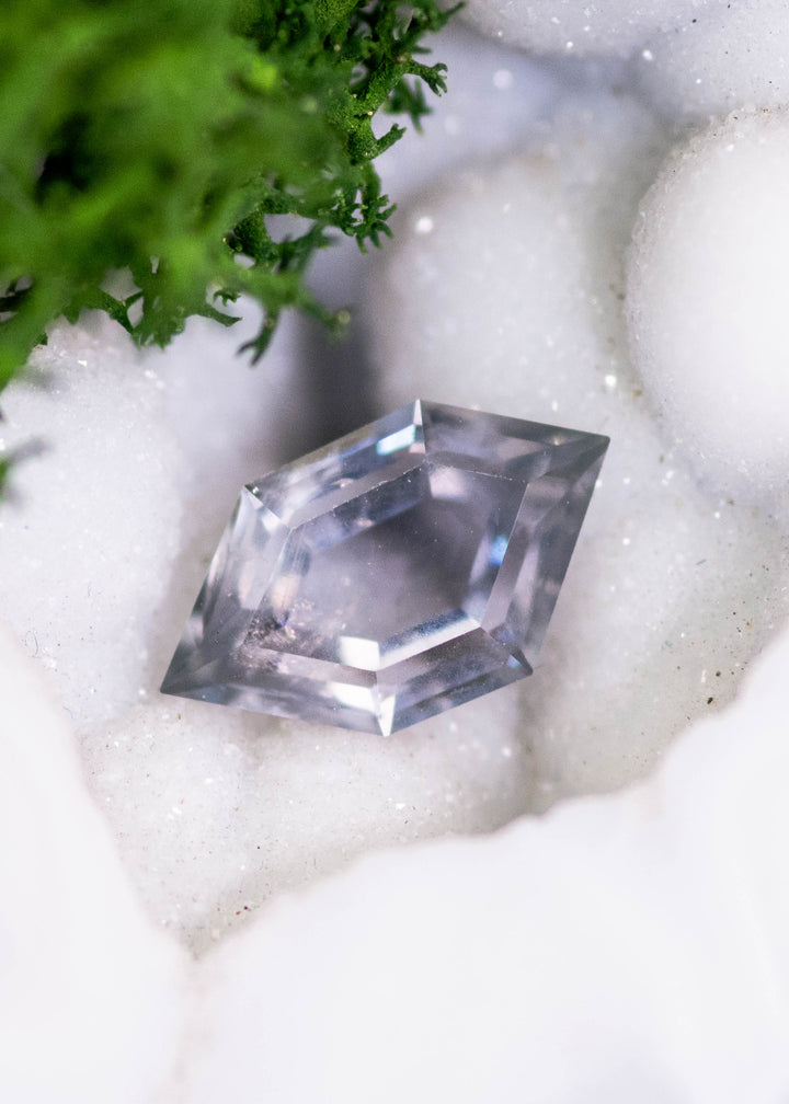 1.03 carat Montana sapphire in blue, purple, and gray tones displayed on white crystal matrix, hexagon portrait cut showing step facets and natural color zoning from El Dorado Bar Deposit, untreated.