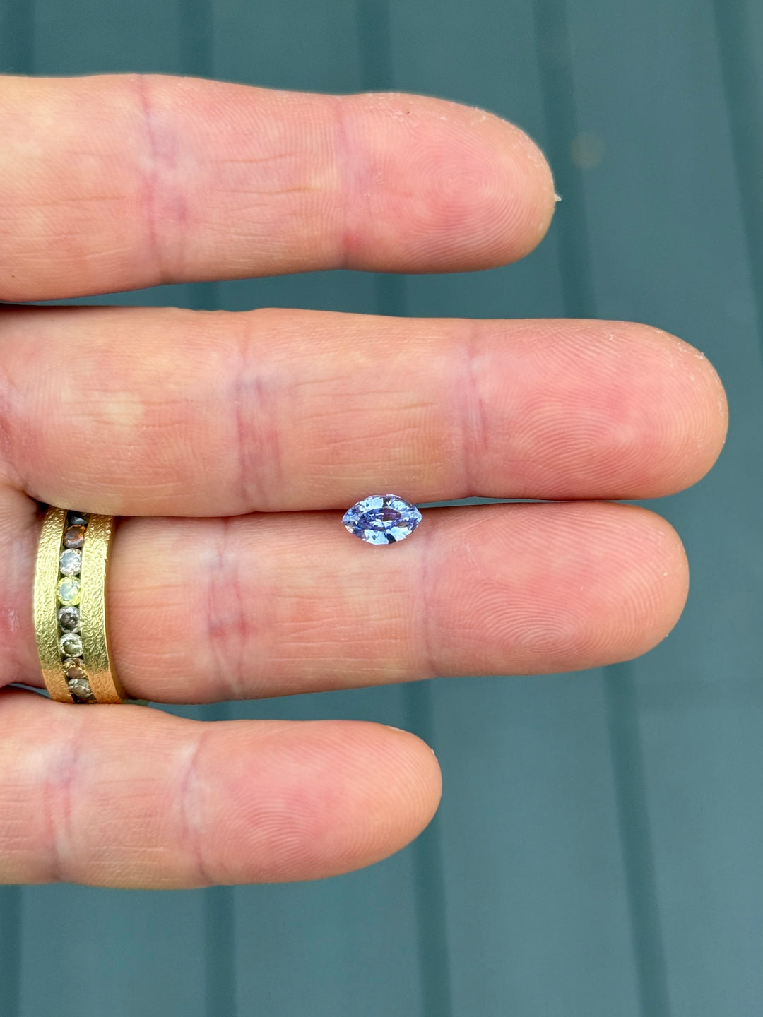 1.03 carat indigo and purple sapphire displayed on fingertips, revealing elegant symmetry, saturation, and sparkle of the precision marquise mixed cut, untreated sapphire from Sakaraha, Madagascar.
