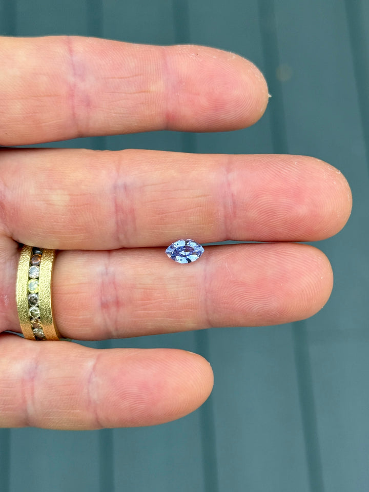 1.03 carat indigo and purple sapphire displayed on fingertips, revealing elegant symmetry, saturation, and sparkle of the precision marquise mixed cut, untreated sapphire from Sakaraha, Madagascar.