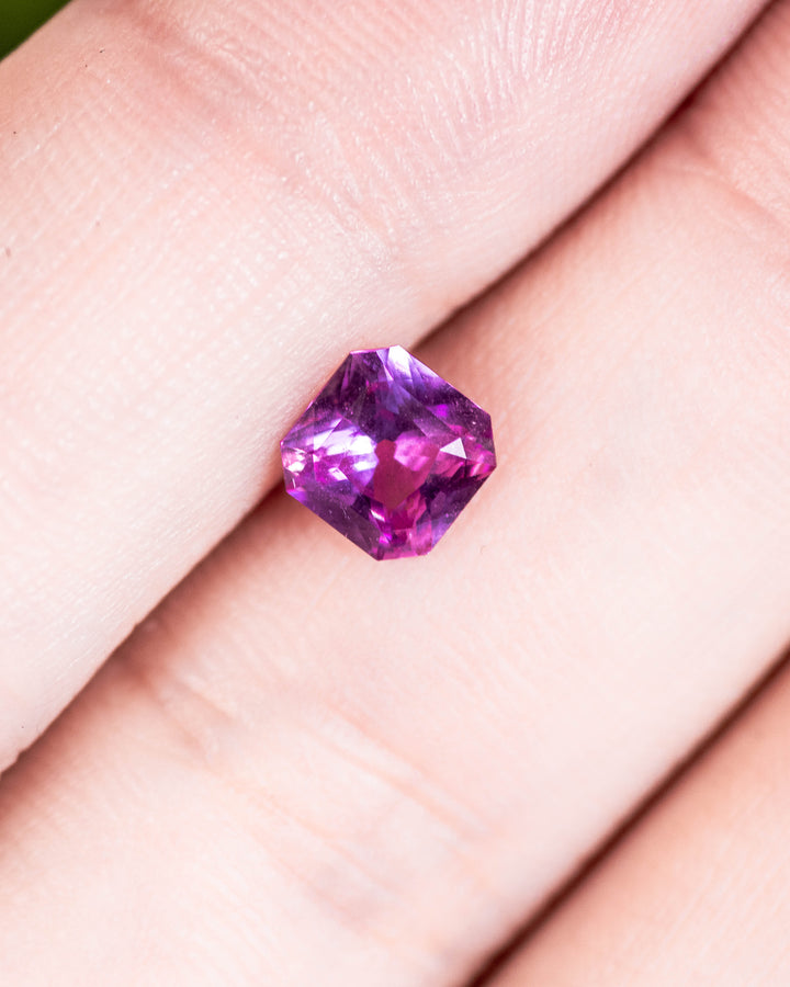 1.03 carat pink and purple sapphire displayed on fingertip, capturing light reflections and vibrant hues from the precision square scissor cut, untreated sapphire from Sakaraha, Madagascar.