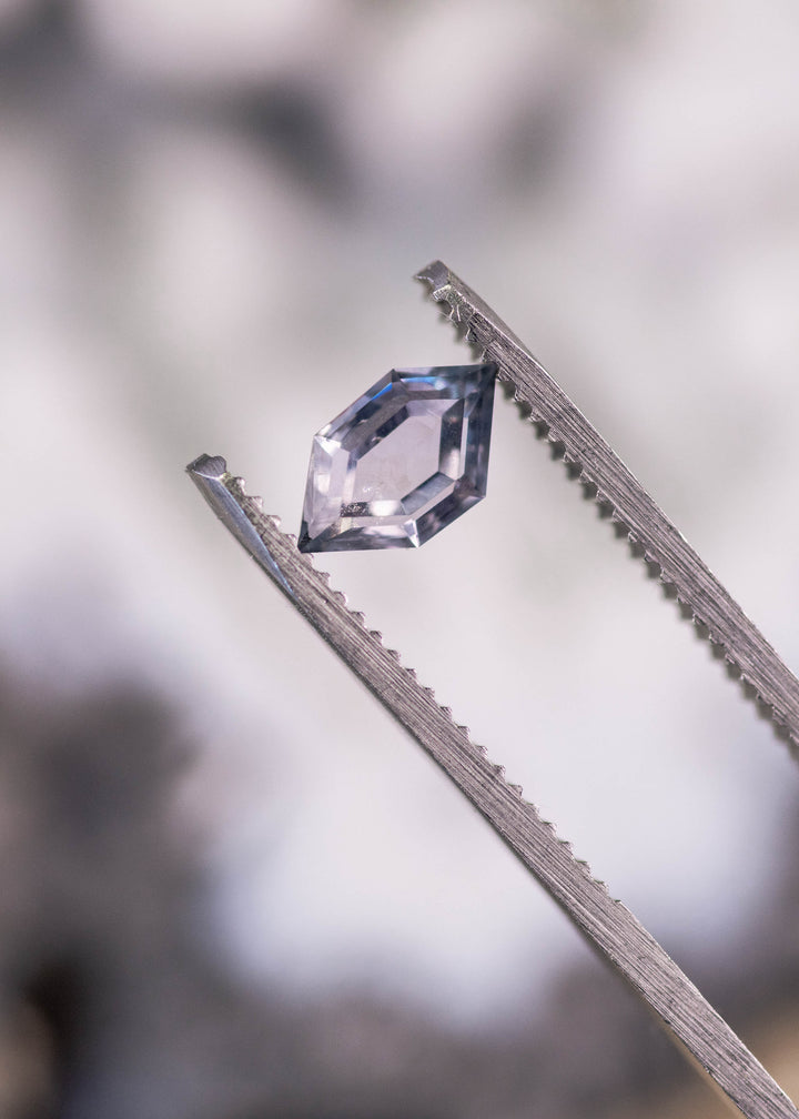 1.03ct untreated Montana sapphire hexagon portrait cut held in gem tweezers, blue purple gray color shifting under light, custom tablet cut from El Dorado Bar Deposit.