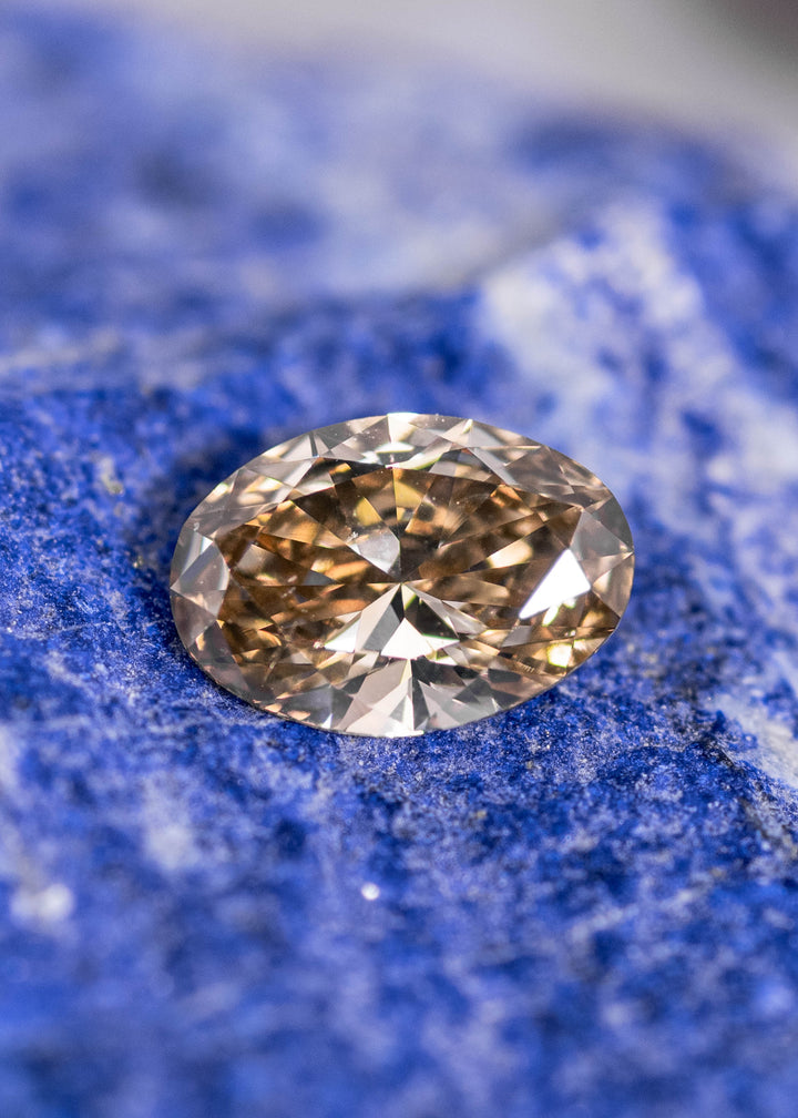 Loose oval brown diamond resting on blue stone showing natural color and brilliance, Canadian diamond gemstone.