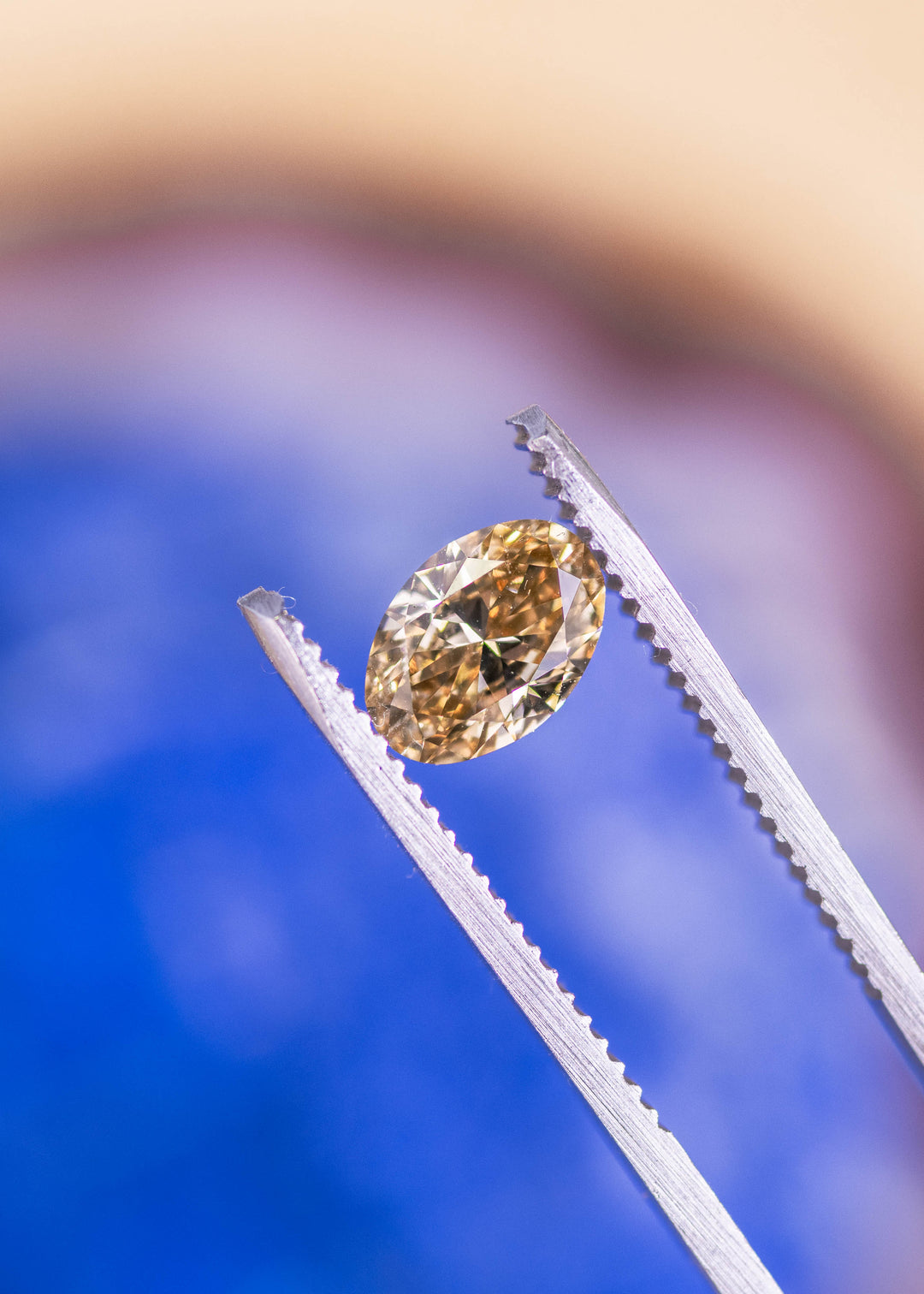 1.03 carat brown oval diamond held in tweezers displaying facet pattern and light reflection, loose diamond.
