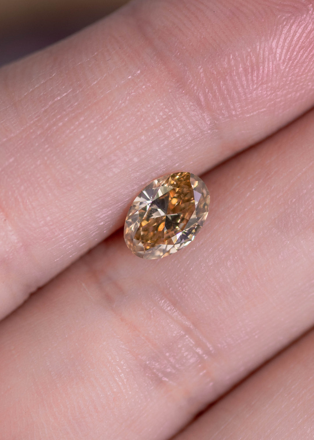 Oval brown diamond on finger showing size and warm earthy tone, loose diamond for engagement ring or jewelry.