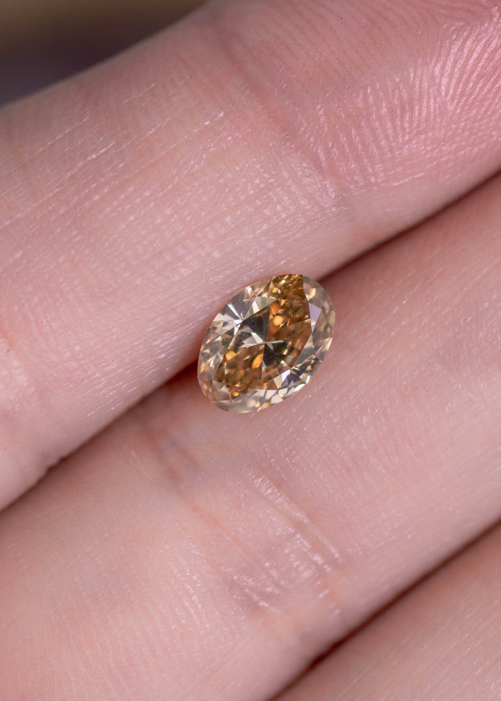 Oval brown diamond on finger showing size and warm earthy tone, loose diamond for engagement ring or jewelry.