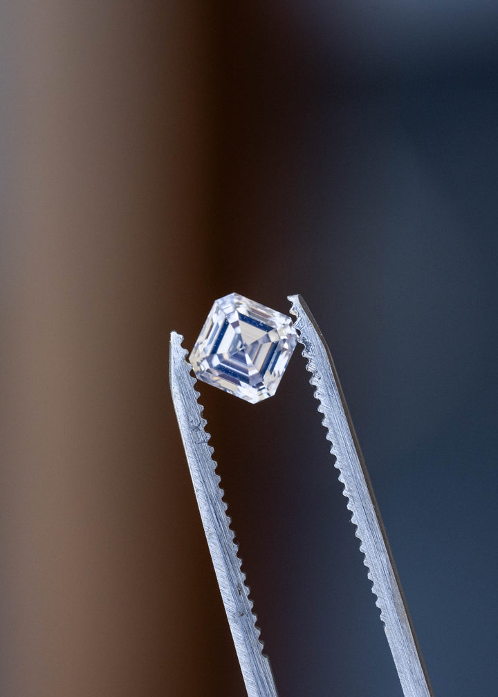 1.03 carat Asscher cut Canadian diamond held at an angle in jeweler’s tweezers against a dark background, displaying geometric depth and mirrored facet reflections.