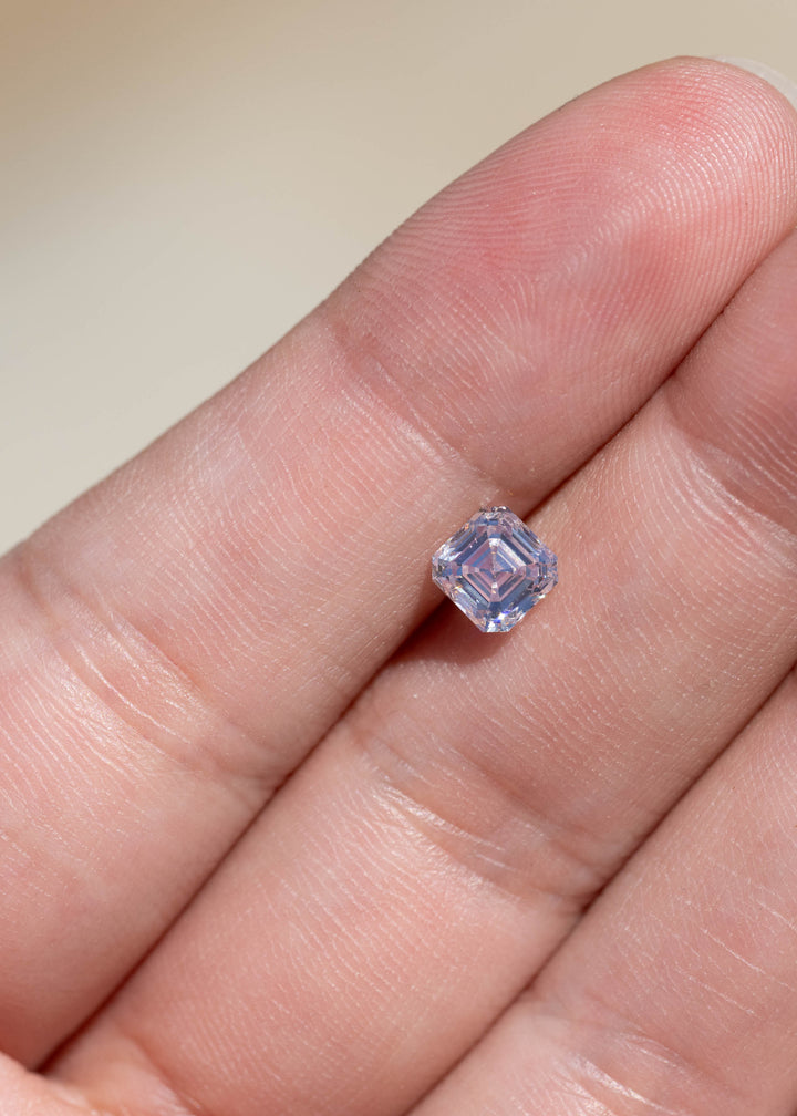 1.03 carat M color VVS1 Asscher cut diamond resting on a hand for scale, with pale champagne and cool silver reflections visible through the step facets.