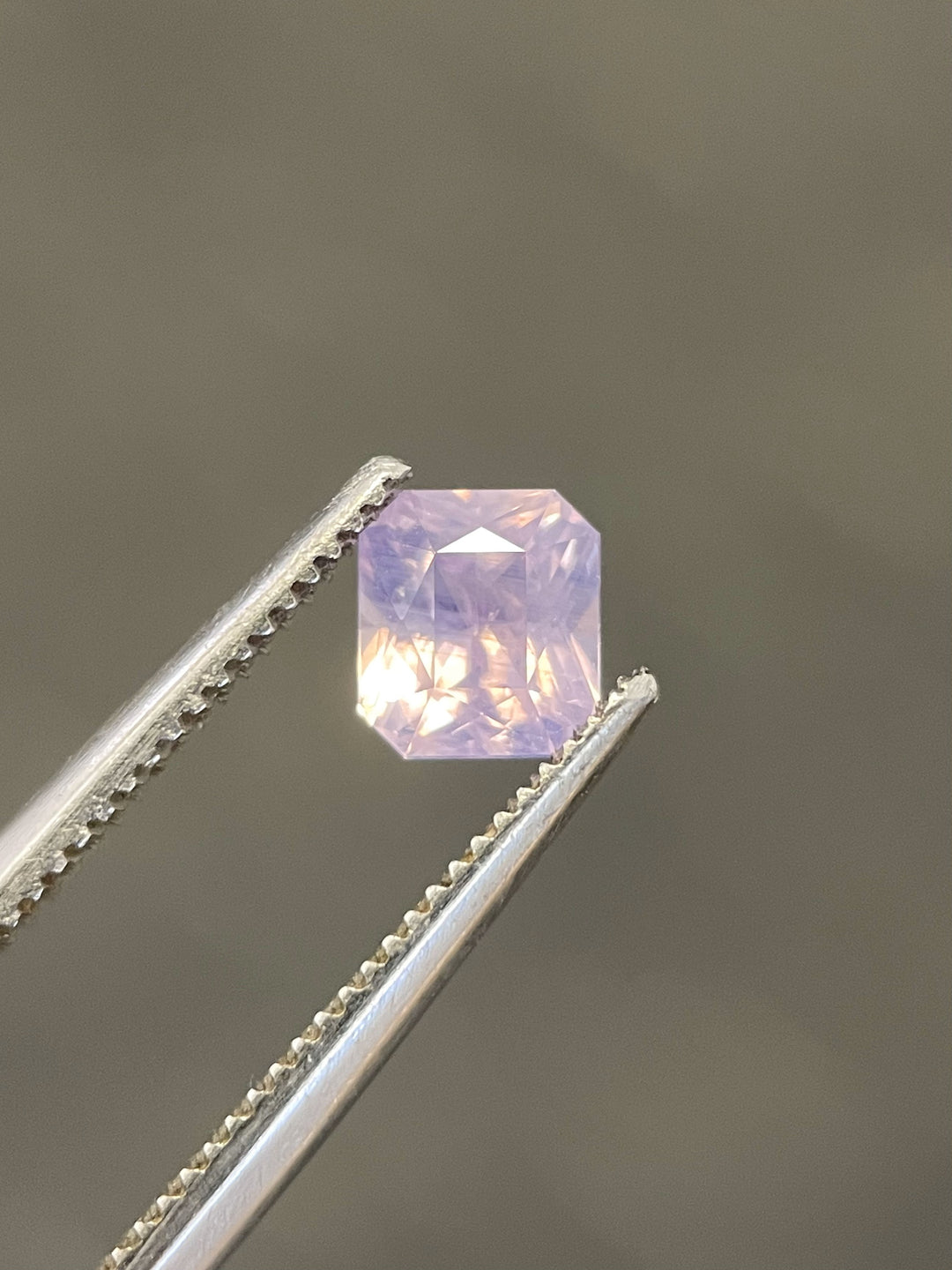 Close-up of a 1.04 carat opalescent sapphire gemstone from Sri Lanka, featuring a cushion cut design with soft pink and purple hues, untreated and elegant.