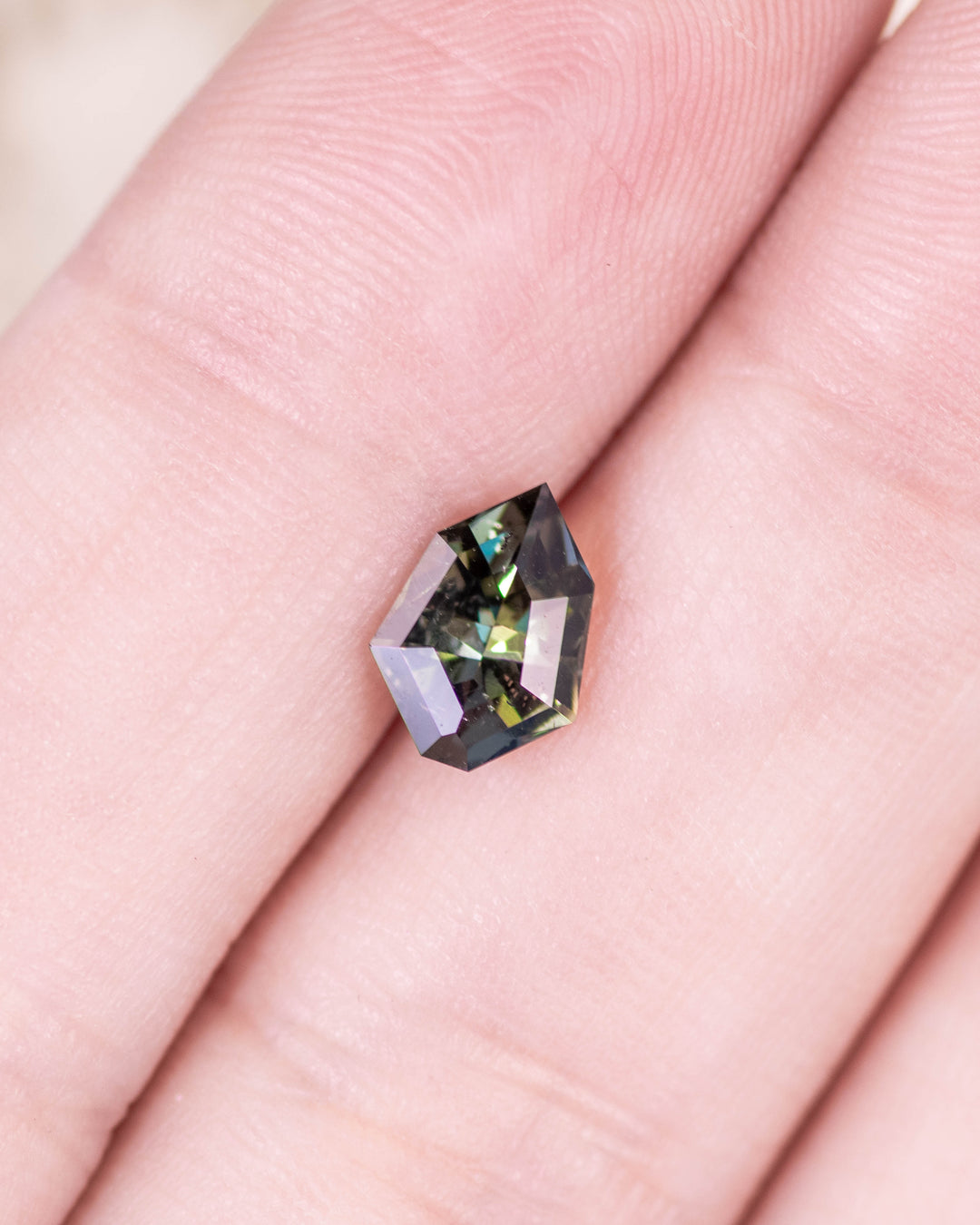 1.05 carat tanzanite displayed on fingertip under natural light, showing the interplay of yellow, green, and blue hues with sharp geometric shield facets, untreated gemstone from Merelani Hills, Arusha Region, Tanzania.