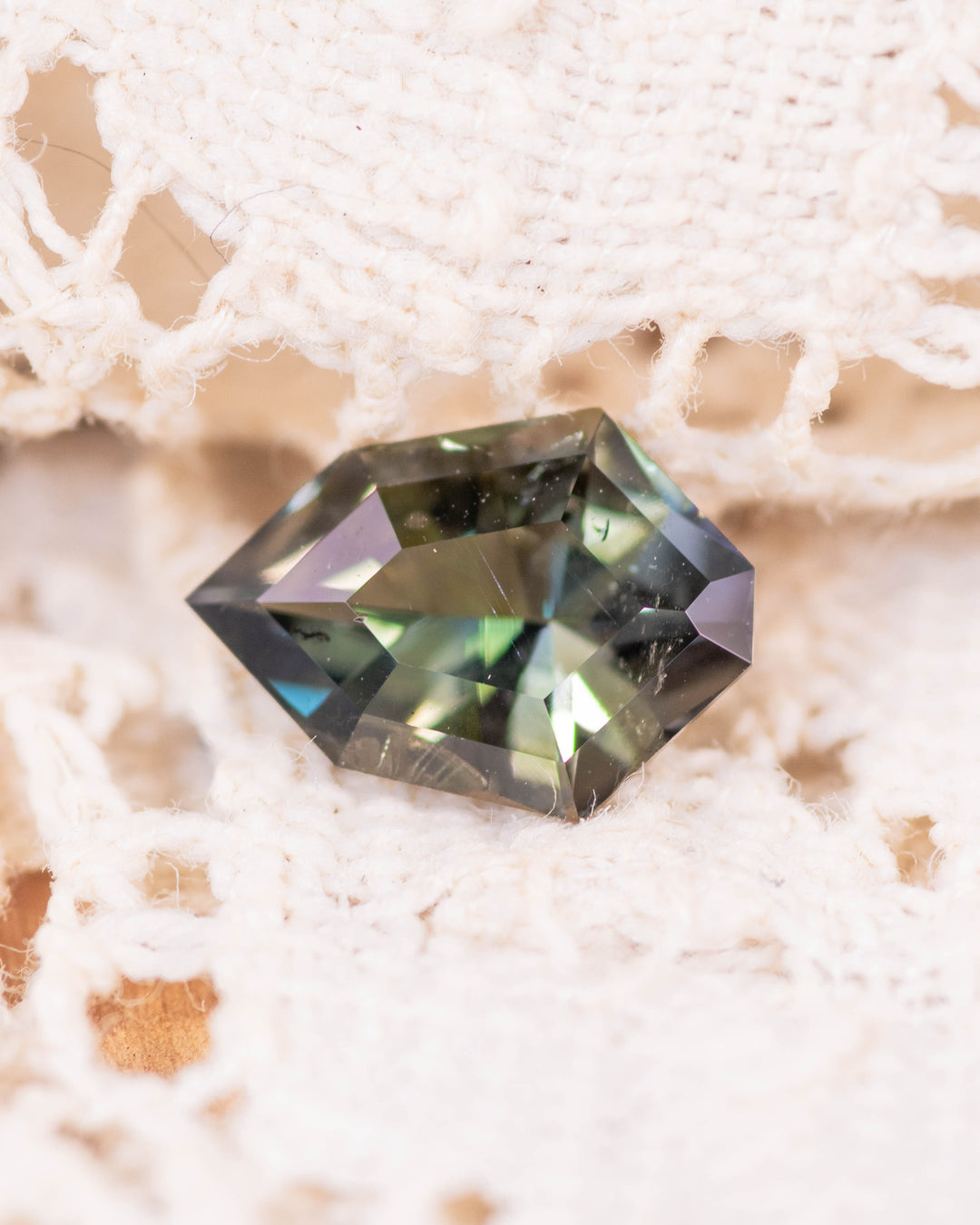 1.05 carat yellow green blue tanzanite resting on soft woven fabric, capturing multicolor reflections through its custom geometric mix cut shield shape, untreated gemstone from Merelani Hills, Arusha Region, Tanzania.
