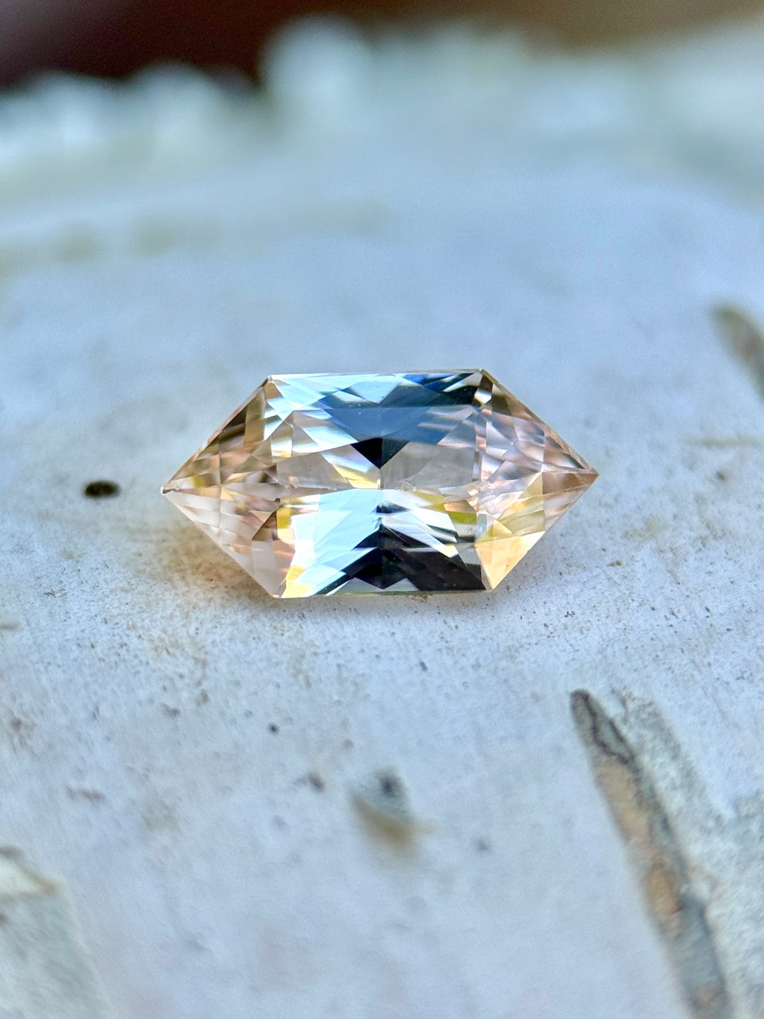 Loose salmon pink peach sapphire elongated hexagon cut resting on natural stone surface, unheated Madagascar gemstone.