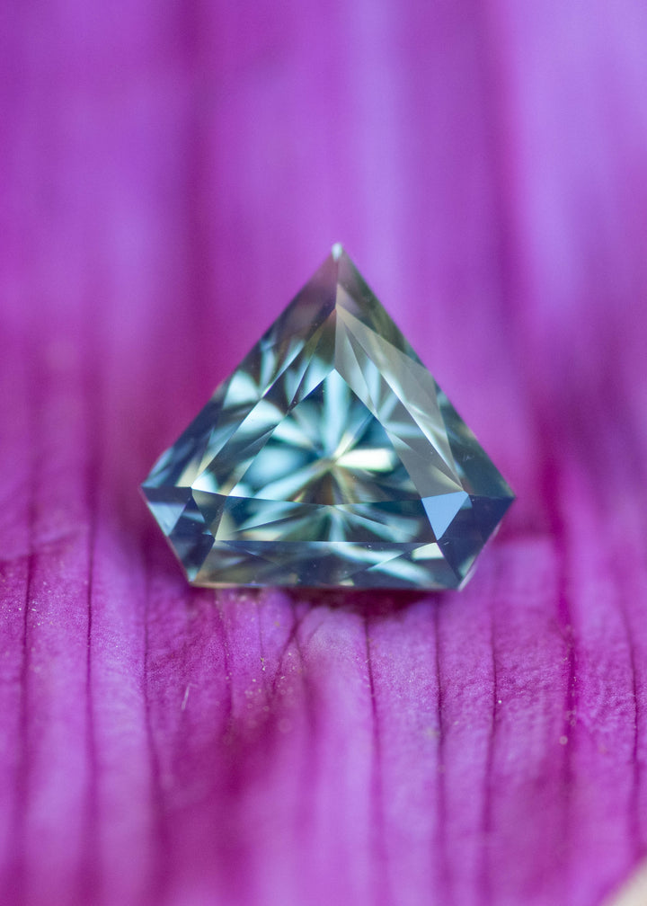 Loose 1.06 carat parti blue green sapphire resting on flower petals showing geometric shield shape and natural Madagascar color zoning.