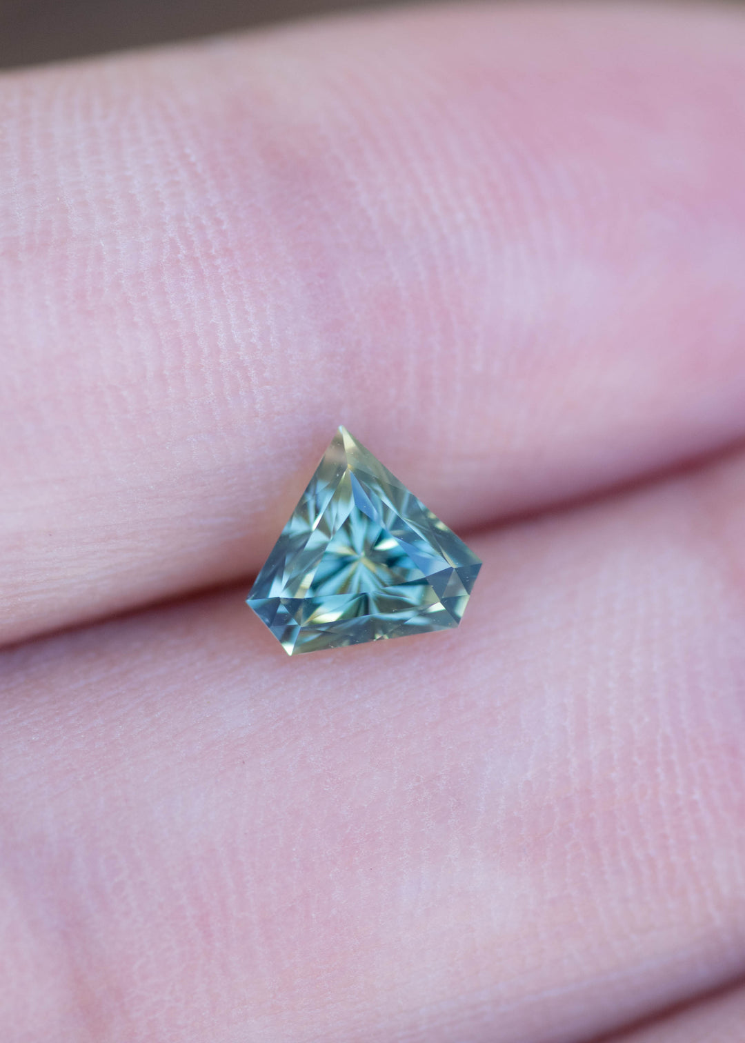 Loose 1.06 carat parti blue green sapphire displayed on hand showing modified shield cut, precision faceting, and natural Madagascar color.
