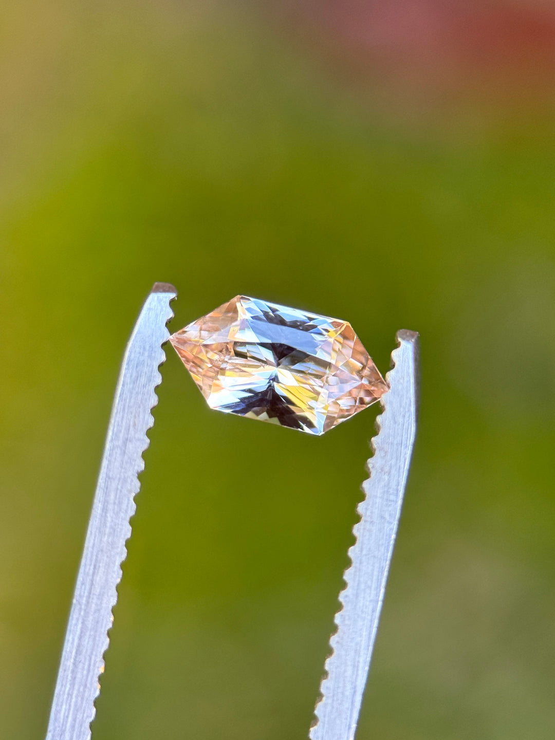 1.06 carat salmon pink peach sapphire held in tweezers showing brilliance and custom hexagon modified cut, loose gemstone.