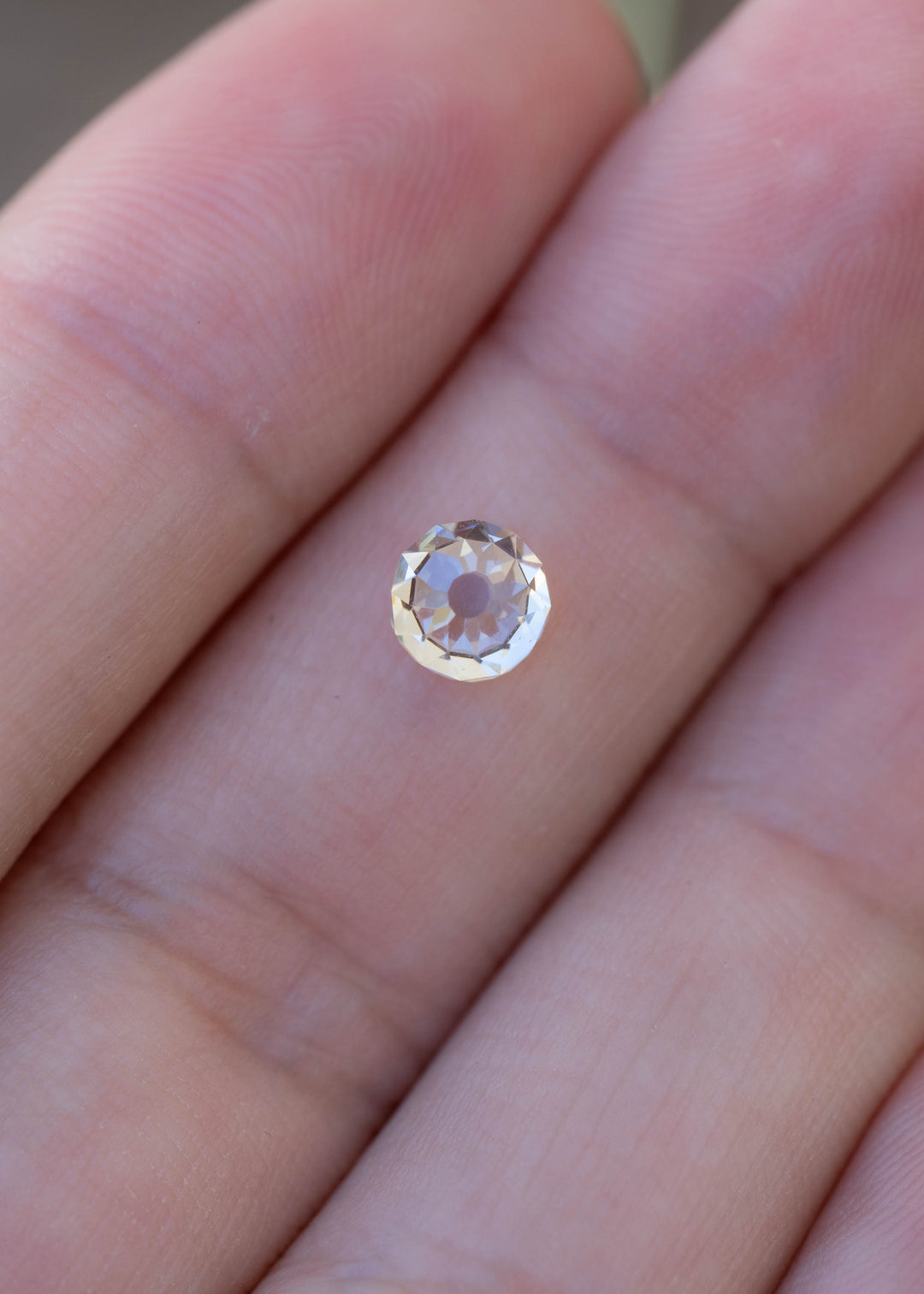 1.06 carat round Mughal cut diamond resting on a fingertip for scale, showing its soft ivory-champagne tone, circular silhouette and antique-style faceting.