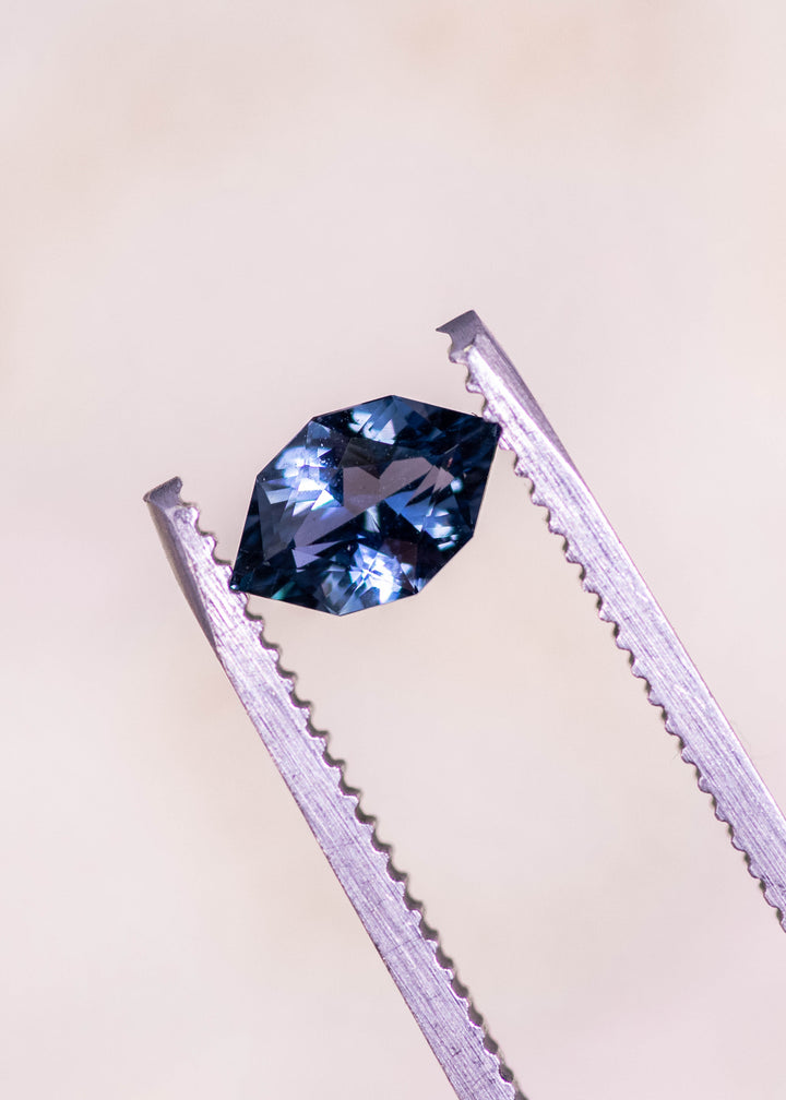 Loose denim blue sapphire held in tweezers, highlighting the elongated modified brilliant marquise cut and rich blue color from Madagascar.