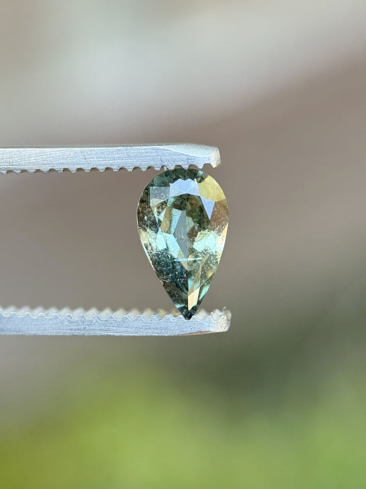 1.06 carat sage teal green sapphire in modified brilliant pear cut held by tweezers, Umba River Tanzania, no heat treatment