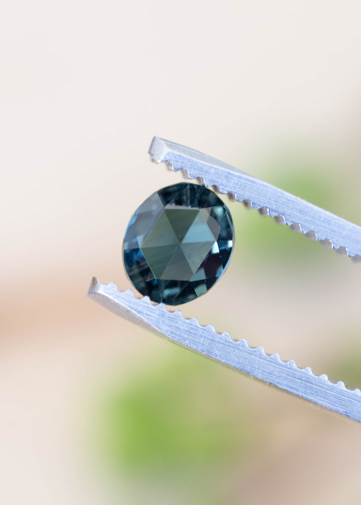 Natural unheated Madagascar teal sapphire held in tweezers displaying rose cut facets