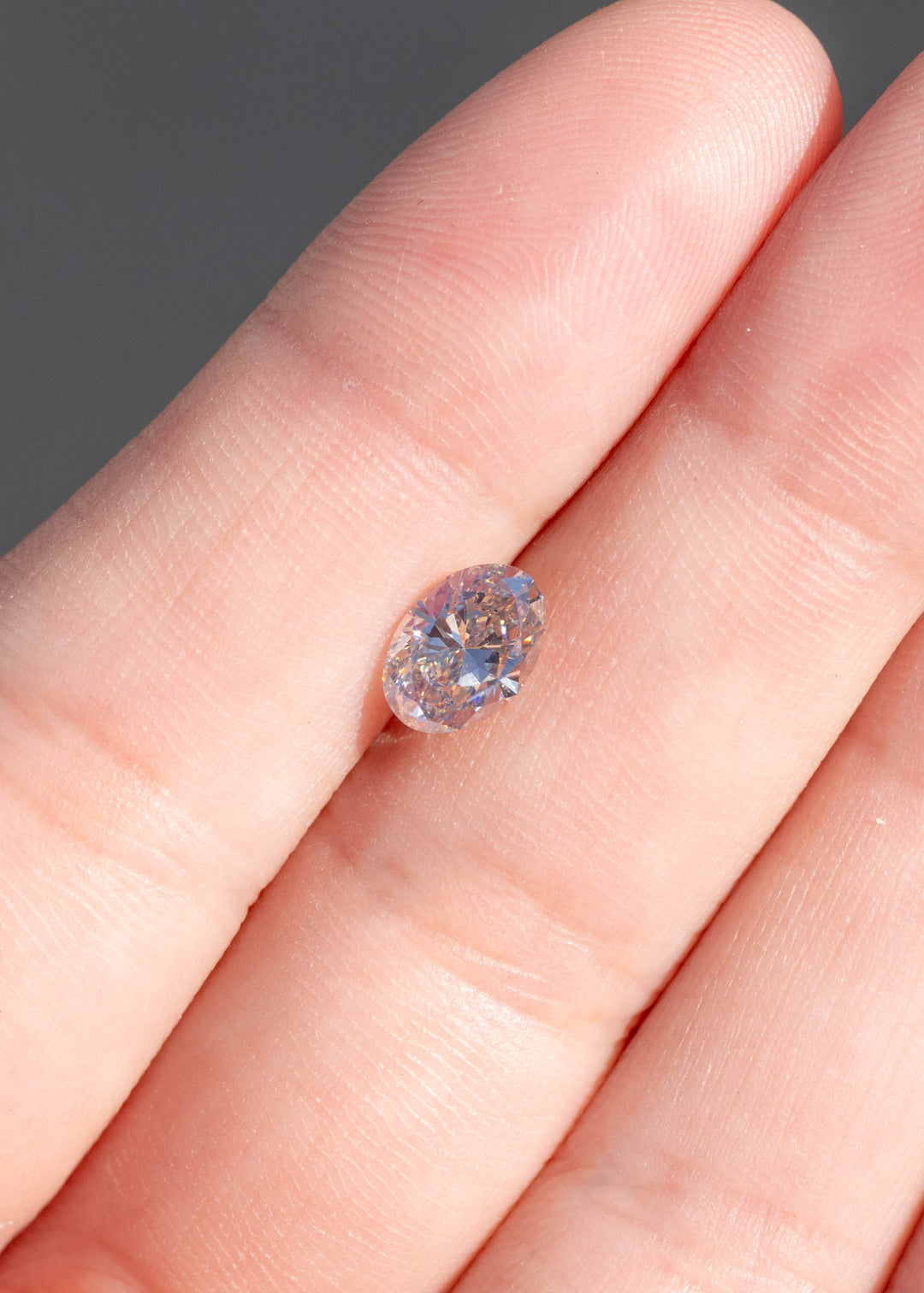 1.07ct natural champagne oval brilliant cut diamond from Canada resting on fingertips showing scale under direct sunlight.