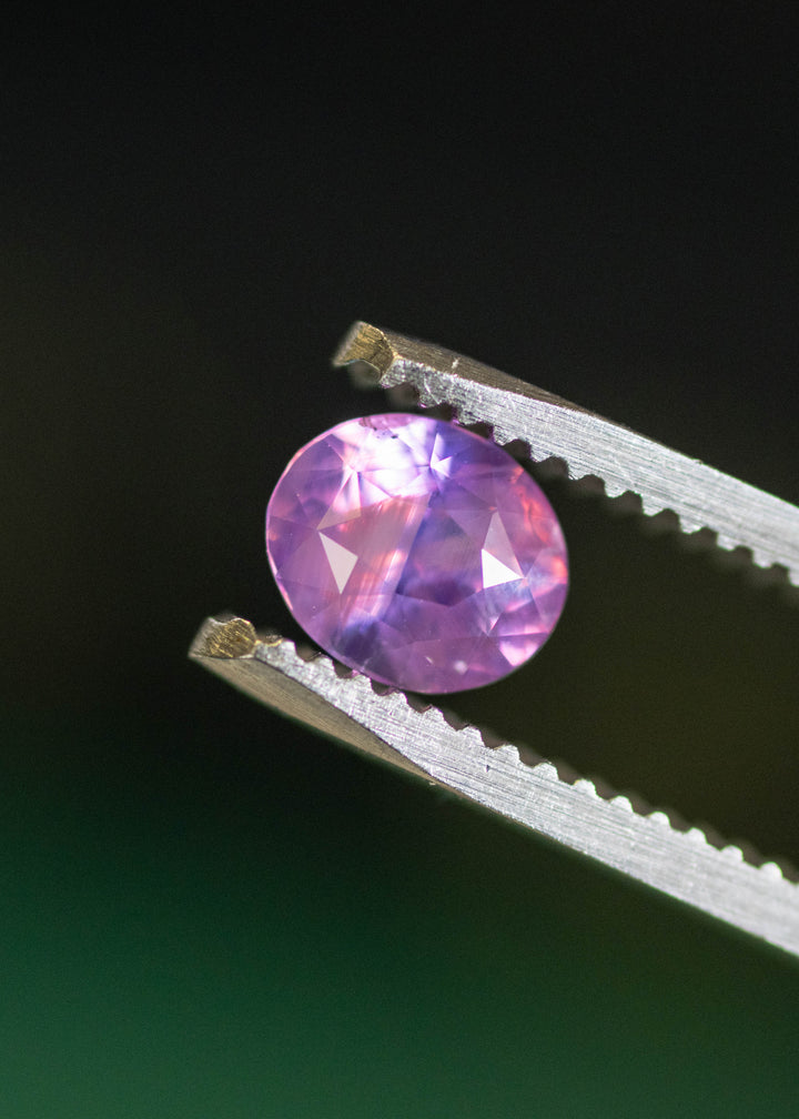 Unheated 1.08ct purple pink sapphire held in tweezers, displaying crisp facet junctions, lavender-pink color blending, and subtle internal silk characteristic of Ratnapura sapphires.