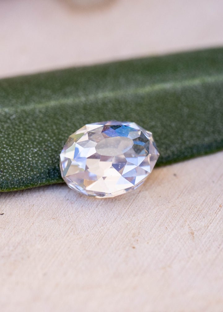 1.08 carat oval Mughal cut South African diamond resting beside a green leaf, showing its elongated outline, broad central table and irregular antique-style faceting.