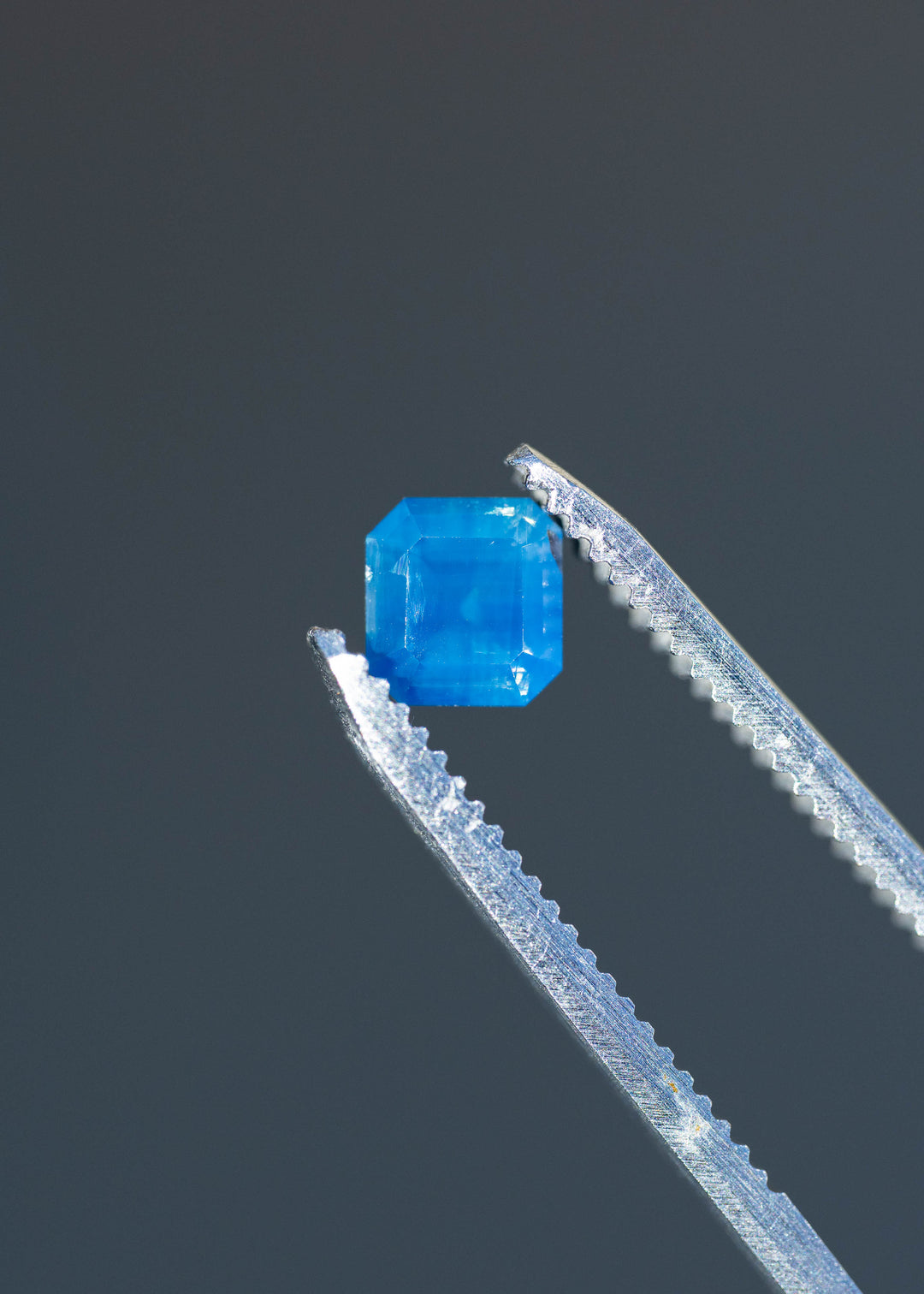 Detailed photograph of an untreated opalescent denim blue sapphire from Gombe, Nigeria. The stone's compact octagonal outline and rich blue color are shown against a dark gray background.