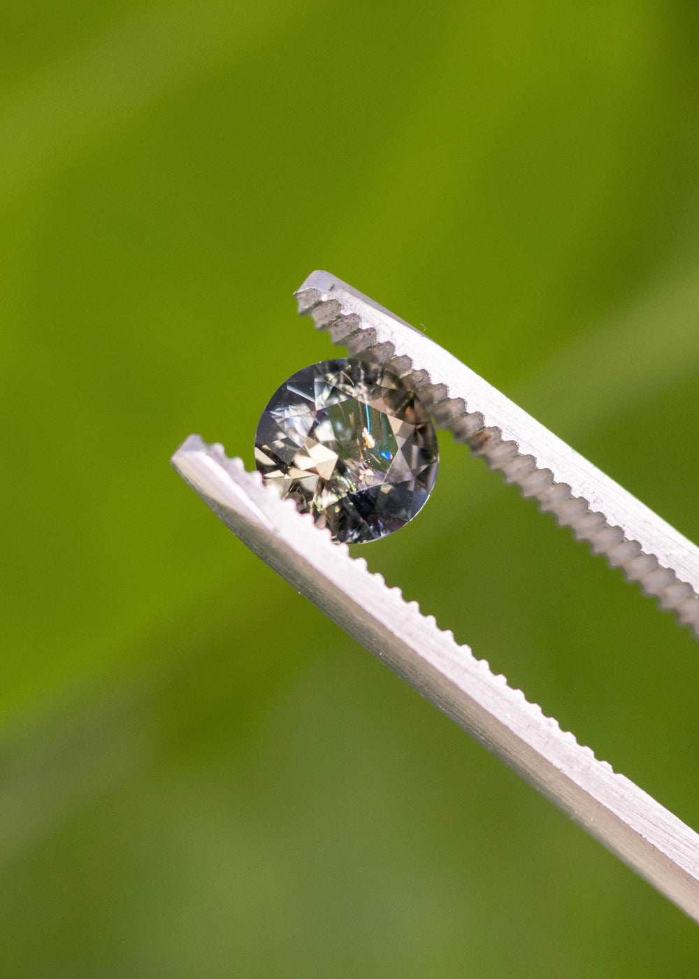 1.08ct blue and brown tanzanite custom modified round brilliant held in gem tweezers, highlighting sparkle, crown facets, and natural untreated gemstone from Merelani Hills Tanzania.