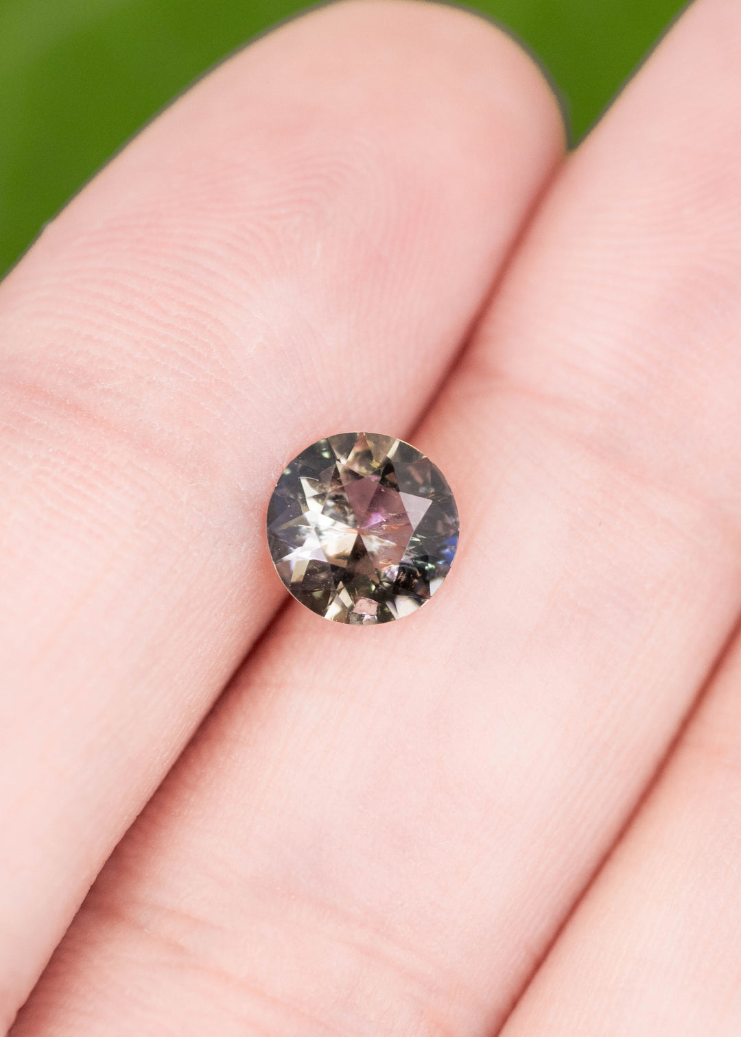 1.08 carat blue and brown tanzanite custom modified round brilliant cut displayed on fingertips, showing precision faceting and natural color shift for custom jewelry design.