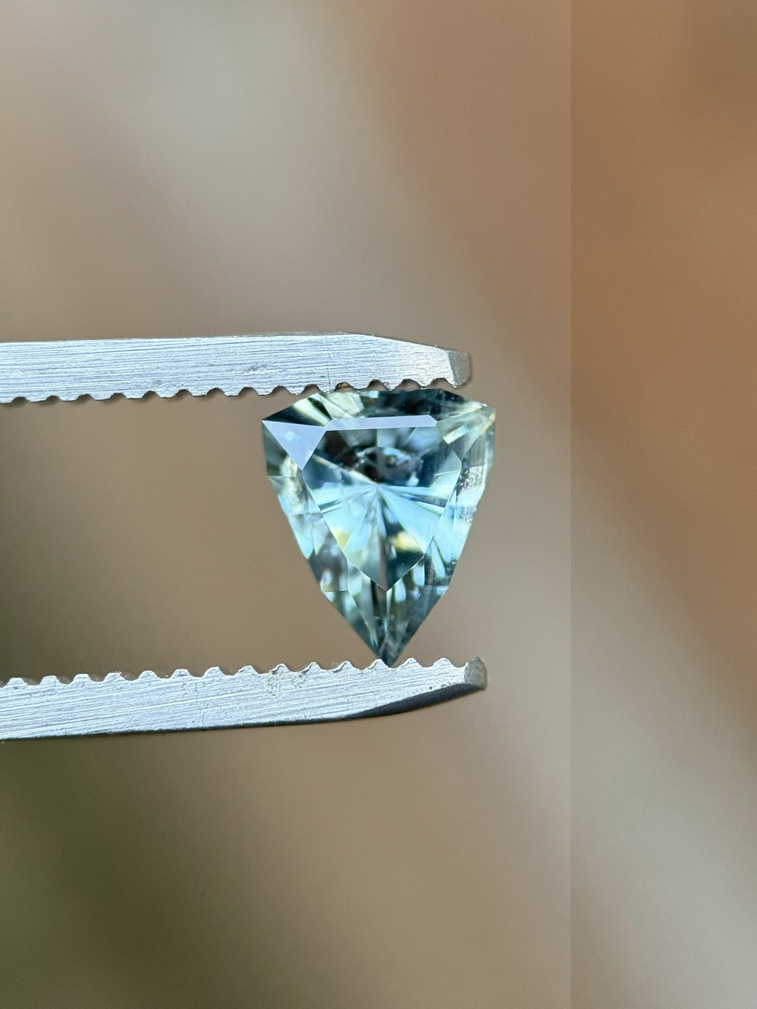 Side view of 1.08ct custom shield cut sapphire held in tweezers, showing sky blue and teal tones, untreated from Malawi.