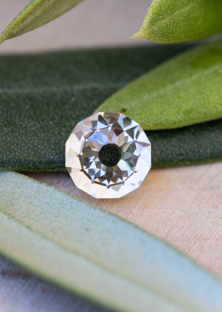 Close-up of a 1.09 carat Mughal cut diamond resting among leaves, revealing its near-round outline and mosaic of white, champagne and silvery blue reflections.